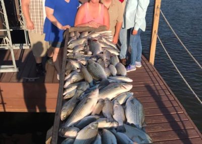 A group of people standing on the dock with fish.