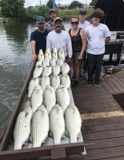 A group of people standing next to a boat filled with fish.