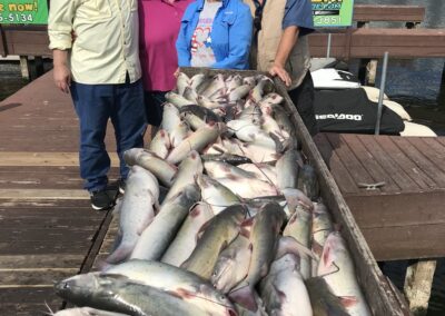 A group of people standing next to a boat filled with fish.