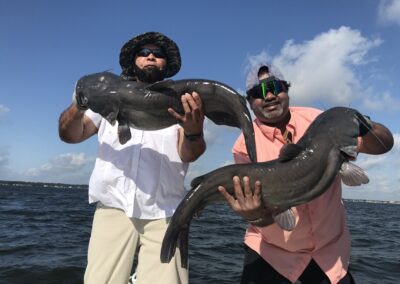 Two men holding large fish in front of the ocean.